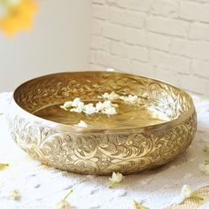 a gold bowl sitting on top of a table next to white flowers and a brick wall