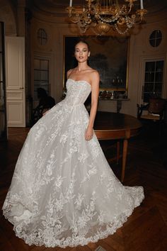 a woman in a white wedding dress standing on a wooden floor next to a chandelier