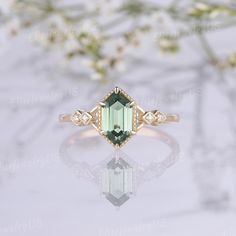 an emerald colored ring with diamond accents on the shoulders and sides, sitting in front of white flowers