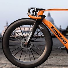 an orange and black bike parked on the side of a road with buildings in the background