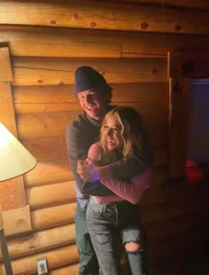 a man and woman hugging in front of a wooden wall with a lamp on it