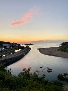 a river running through a lush green hillside next to the ocean under a pink sky