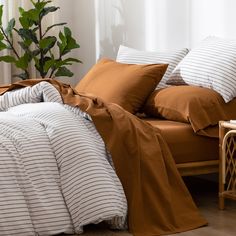 an unmade bed with brown and white striped comforter on it, next to a plant