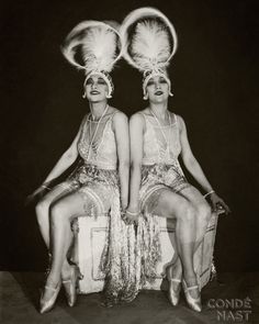 two women sitting next to each other on top of a white chair with silver sequins