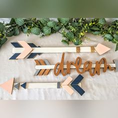 a wooden sign that says dream with arrows and greenery on the table next to it