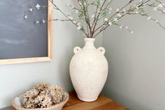 a white vase sitting on top of a wooden table next to a bowl with flowers in it