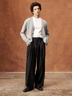 a man standing in front of a brown wall wearing black pants and a white shirt