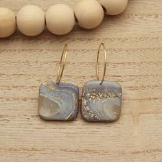 two square shaped earrings on top of a wooden table