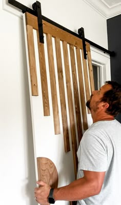 a man holding a piece of wood in front of a sliding door with wooden slats on it