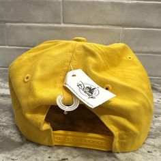 a yellow hat with a tag on it sitting on the ground next to a brick wall