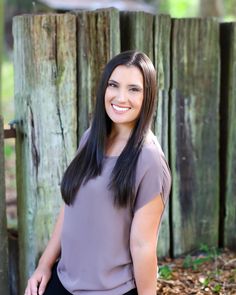 a woman sitting in front of a wooden fence with her hands on her hips and smiling at the camera