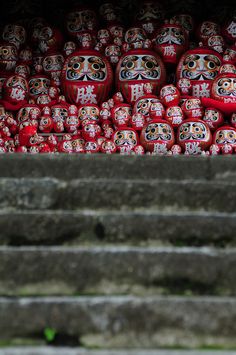 many red dolls are stacked on top of each other in front of some stone steps