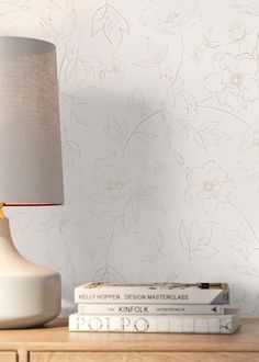 a lamp on a table next to books and a vase with flowers painted on it