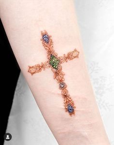 a woman's arm with a cross tattoo on it, decorated with multicolored stones