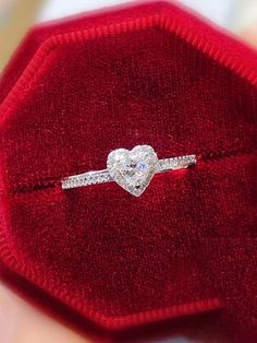 a heart shaped diamond ring sitting on top of a red velvet case