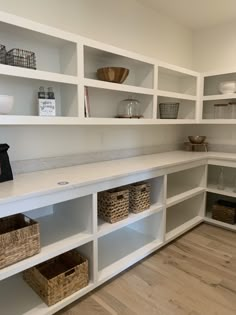 a kitchen with white shelves and baskets on the counter top, in front of a wooden floor