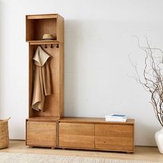 a wooden cabinet with clothes hanging on it and a basket next to it, in front of a white wall