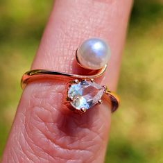 a close up of a person's hand holding a ring with a pearl on it