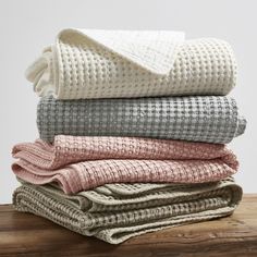 folded blankets stacked on top of each other in various colors and patterns, sitting on a wooden surface