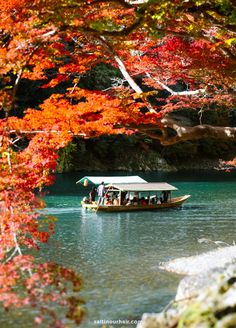 a boat with people on it is in the middle of a lake surrounded by fall colored trees