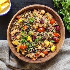 a wooden bowl filled with rice and vegetables next to some sliced up lemon wedges