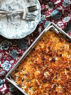 a casserole dish on a floral table cloth next to two plates with silverware