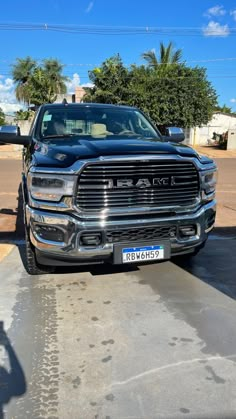 the front end of a black ram truck parked in a parking lot with palm trees behind it