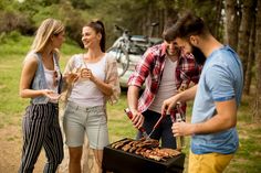 group of people standing around a bbq grill with food on it and wine glasses in their hands