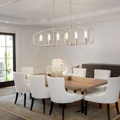 a dining room table with white chairs and a chandelier hanging from the ceiling