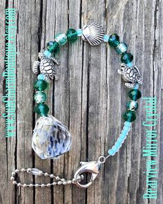 a bracelet with green glass beads and silver charms on a wooden background that says mermaid