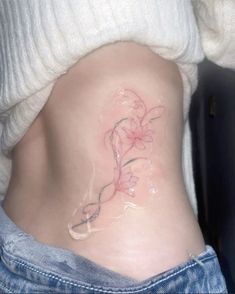 a woman's stomach with a tattoo on the side that has flowers and vines drawn on it