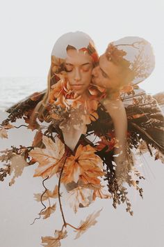 a man and woman standing next to each other in front of leaves on the ground