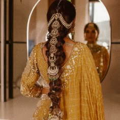 a woman with long hair in a yellow dress looking at her reflection in a mirror