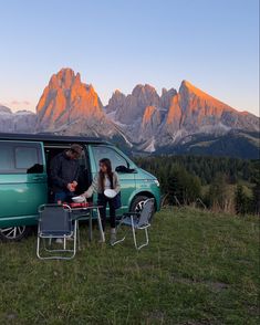 two people sitting at a table in front of a van with mountains in the background