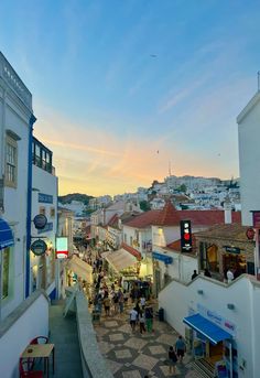 people are walking around in the city at sunset or dawn, with shops and restaurants on either side