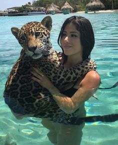 a woman is holding a large leopard in the water