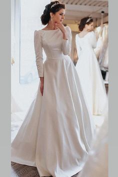 a woman standing in front of a mirror wearing a white wedding dress with long sleeves