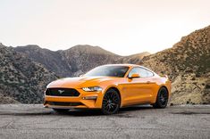 an orange ford mustang parked in front of mountains