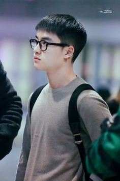 a young man with black glasses and a gray shirt is standing in an airport terminal