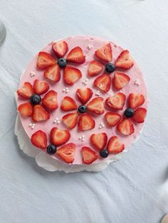 there is a cake with strawberries and blueberries on the top it sits on a white table cloth