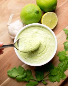 a person spooning guacamole into a bowl with limes and cilantro