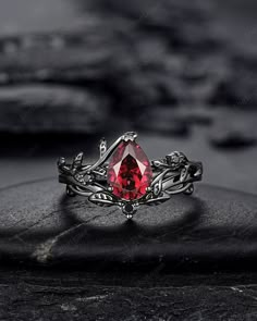 a ring with a red stone in the middle on top of a black rock next to some rocks