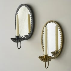 two wall sconces with candle holders and mirrors on the wall in front of them