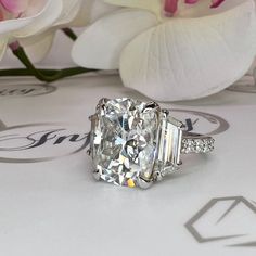 an oval and baguette cut diamond ring on top of a table with flowers