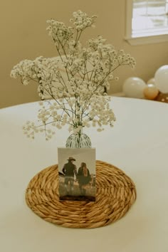 a vase filled with white flowers sitting on top of a wicker tablecloth covered table