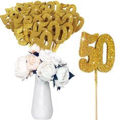 a white vase filled with flowers next to a gold number 50 cake topper on a stick