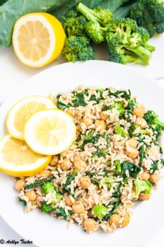 a white plate topped with rice, broccoli and lemon wedges next to greens