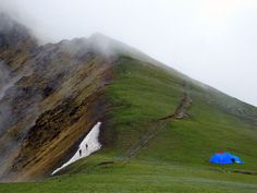 a blue tent sitting on the side of a green mountain next to a snow covered slope