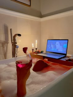 a laptop computer sitting on top of a bath tub filled with water next to candles