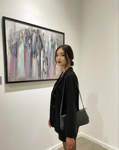 a woman standing in front of a painting on the wall next to a purse and handbag